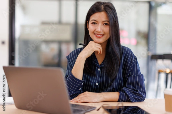 Fototapeta  Asian businesswoman sits at desk with laptop online using internet and notepad happily recording receipt contact information online delivery.
