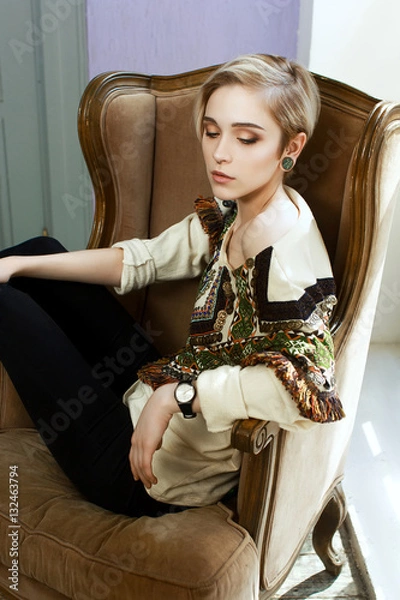 Fototapeta Beautiful girl in a clothes with an ethnic pattern, sitting in a chair in front of a window