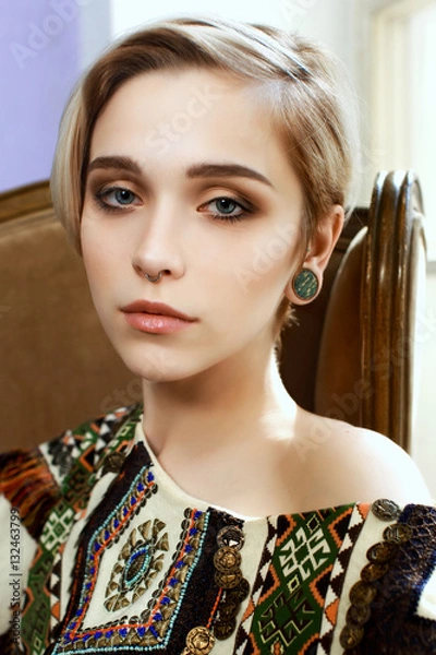 Fototapeta Beautiful girl in a clothes with an ethnic pattern, sitting in a chair in front of a window