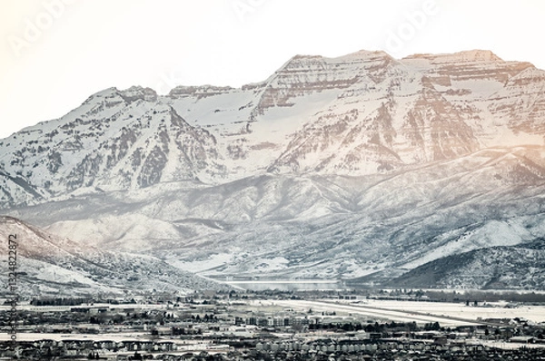 Fototapeta Snow covered mountain range towering over a suburban city in winter