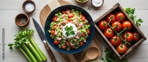 Fototapeta Salad featuring celery, tomatoes, and tuna. Ingredients for the salad laid out on a light wooden table during the cooking process.