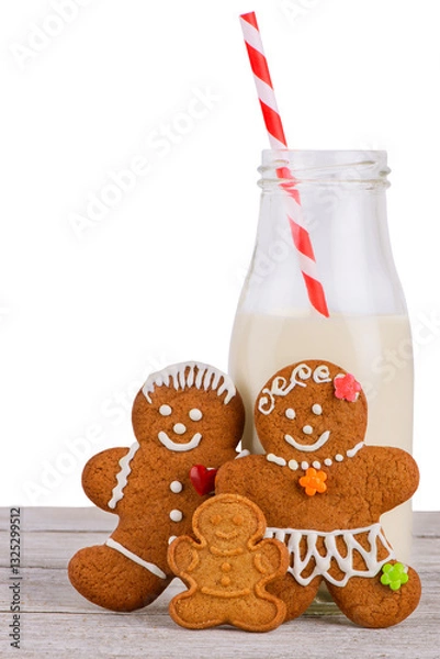Fototapeta Festive gingerbread cookies with icing details and a milk bottle with a red striped straw on a wooden table. A warm and cozy holiday setting perfect for Christmas-themed designs and advertisements.