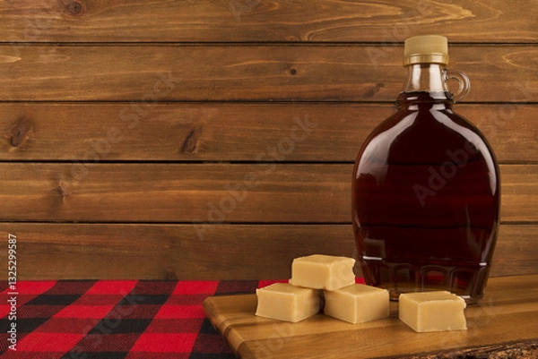 Obraz Bottle of rich maple syrup with golden fudge pieces on a wooden surface, set against a rustic wooden backdrop. A warm, inviting scene capturing the essence of Canadian cuisine and sweet indulgence.