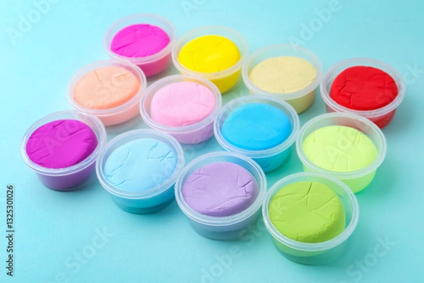 Fototapeta Different colorful modeling clay in plastic jars on light blue background