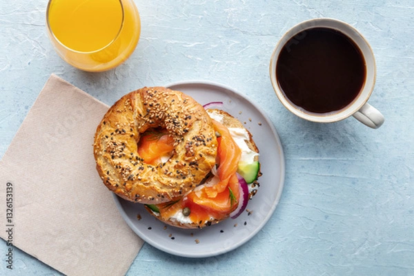 Fototapeta Lox bagel. A breakfast of a sandwich with smoked salmon and fresh vegetables on a plate, with orange juice and coffee, shot from the top