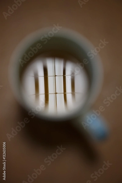 Fototapeta Fluorescent tube reflection in a white cup of tea on brown table. Top view