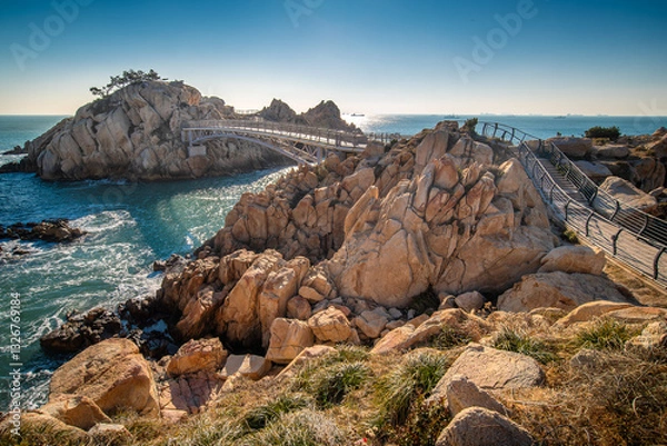 Fototapeta Rocky cliffs of the sea of Japan coast in Korea with a pedestrian bridge leading to an island with clear blue sky and the sun 