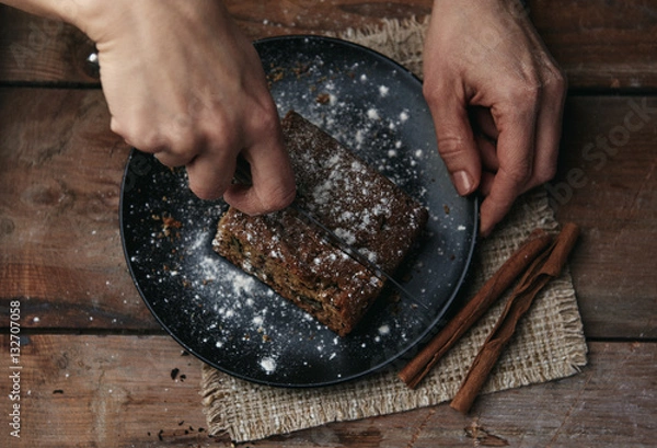 Obraz Close-up of plate with delicious dessert on wooden background. Woman cutting cake piece in rustic kitchen.  