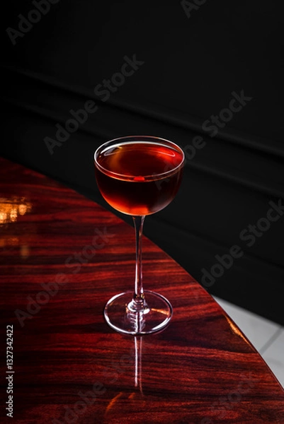 Fototapeta A manhattan cocktail in a coupe glass on glossy wooden table in a bar with copy space