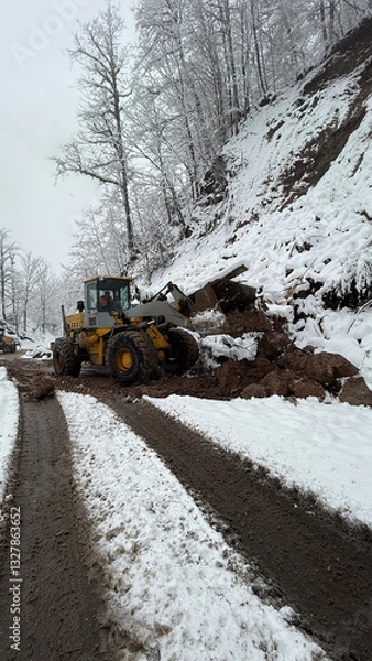 Fototapeta A heavy-duty loader clears a snow-covered mountain road, pushing through thick mud and ice