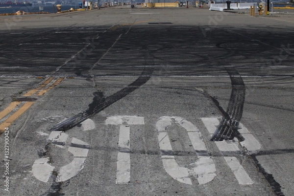 Obraz Cracked asphalt road with a large white stop sign and tire skid marks at an urban intersection emphasizing traffic safety and road conditions