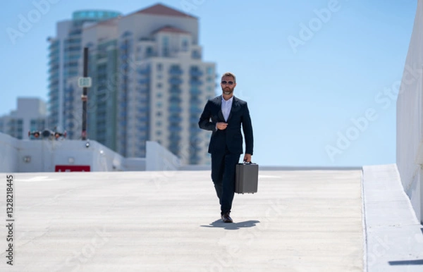 Fototapeta Rich businessman walking outdoors. Successful businessman with briefcase. Corporate leader on the move. Business man walking confidently. Businessman going to work. Handsome businessman in a suit.