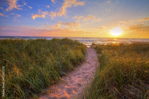 Obraz Ścieżka Do Letniej Plaży Zachodu Słońca. Kręta ścieżka przez trawę wydmową prowadzi do plaży o zachodzie słońca na wybrzeżu śródlądowego morza jeziora Michigan. Park Stanowy Hoffmaster. Muskegon w stanie Michigan.