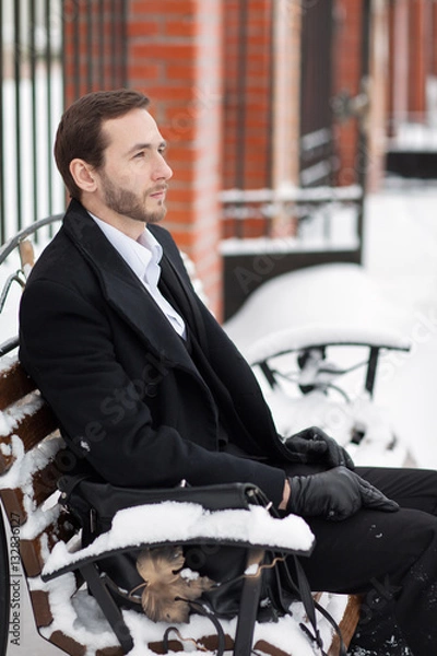 Fototapeta Male businessman sitting on a bench, holding a business briefcase with documents, in the winter on the street