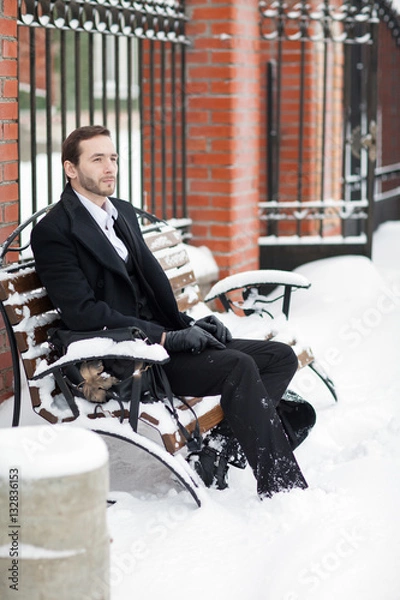 Fototapeta Male businessman sitting on a bench, holding a business briefcase with documents, in the winter on the street