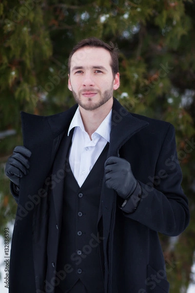 Fototapeta Male businessman sitting on a bench, holding a business briefcase with documents, in the winter on the street