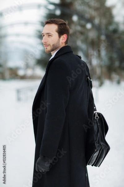 Fototapeta Male businessman sitting on a bench, holding a business briefcase with documents, in the winter on the street