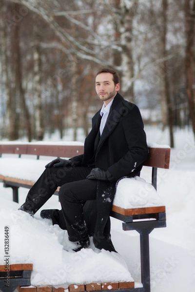 Fototapeta Male businessman sitting on a bench, holding a business briefcase with documents, in the winter on the street