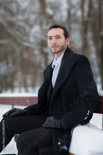 Fototapeta Male businessman sitting on a bench, holding a business briefcase with documents, in the winter on the street
