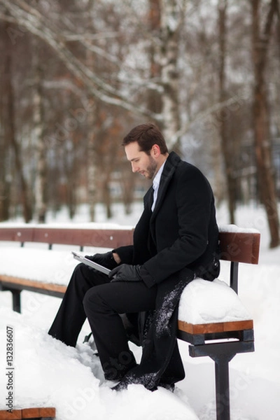 Fototapeta Male businessman sitting on a bench, holding a business briefcase with documents, in the winter on the street