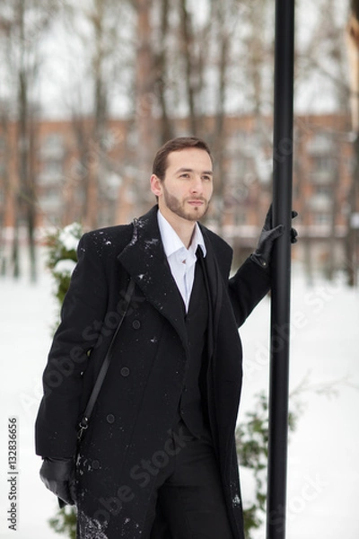 Fototapeta Male businessman sitting on a bench, holding a business briefcase with documents, in the winter on the street