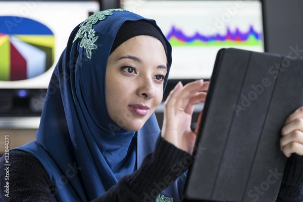 Obraz Young woman wearing a hijab using an ipad/tablet
