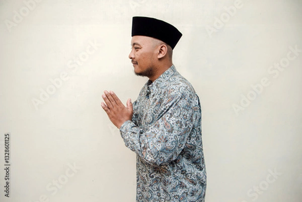 Fototapeta Concept photo of Eid al-Fitr making an apology gesture. Isolated concept photo of an Asian Muslim man making an apology hand gesture during Eid al-Fitr celebration on white background