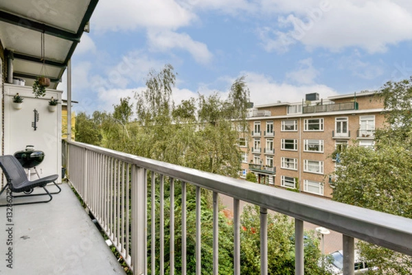 Obraz A beautiful view from a balcony showcasing lush greenery and urban architecture under a clear sky. The space invites relaxation and observation of nature.
