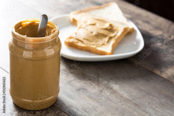 Fototapeta Peanut butter jar and toasts on wooden table. Copyspace.
