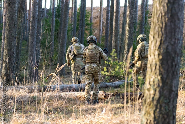 Fototapeta Soldiers in the forest. Military men in camouflage with weapons.