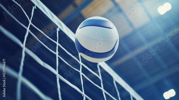 Obraz Low-angle close-up of a white leather volleyball soaring over the net in an indoor volleyball arena during a competitive match, capturing the fast-paced action and intensity of the game.


