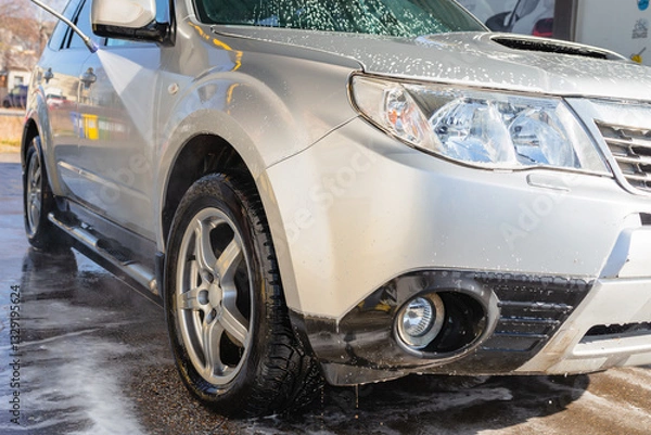 Fototapeta Washing an SUV with high-pressure water and foam at a self-service car wash, cleaning the vehicle exterior on a sunny day