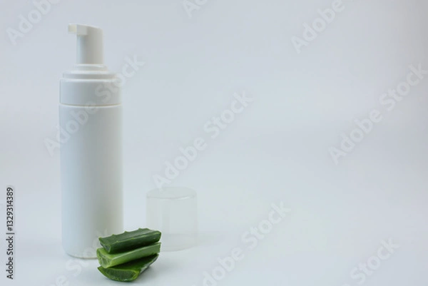 Fototapeta Close-up of a white foam cleanser with a dispenser for nourishing, moisturizing and cleansing the skin stands on a white background, next to it there are aloe leaves with space for text. Body and face