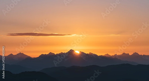 Obraz A golden sunset behind the mountains, with soft clouds glowing in the evening light.