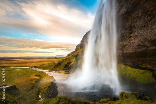 Fototapeta Majestic Seljalandsfoss waterfall cascading down Iceland's lush landscape at sunset