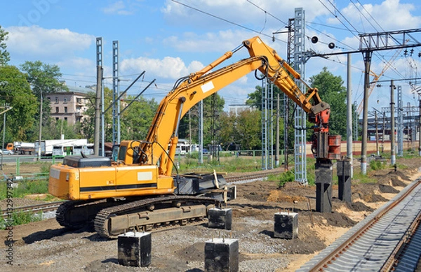 Obraz Экскаватор устанавливает сваю для новой платформы железнодорожной станции 