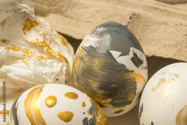 Fototapeta Close-up of beautifully decorated Easter eggs with golden and black paint splashes, surrounded by crumpled paper and an egg carton, perfect for holiday celebrations.