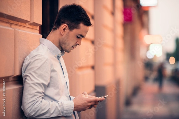 Fototapeta Handsome young man text messaging on a city street