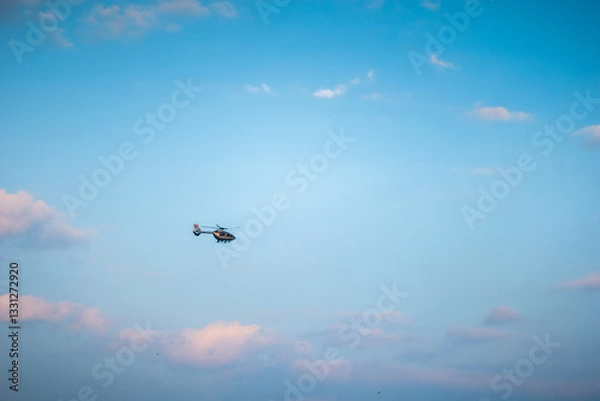 Fototapeta A helicopter flying high in the sky against a backdrop of blue sky and scattered clouds