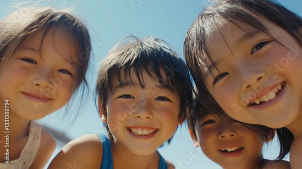 Obraz 日本の小学生・幼稚園児・保育園児4人がカメラを覗き込んで笑っている写真　背景青空　夏