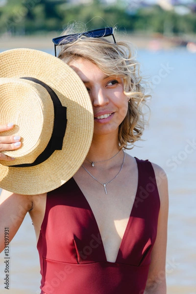 Fototapeta Girl with glasses puts on a hat while relaxing on the beach. Summer mood.