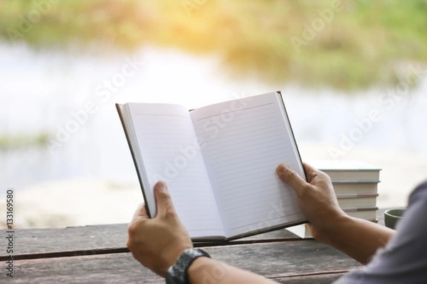 Fototapeta Stock Photo:.Man reading a book and writing notes on wooden tabl