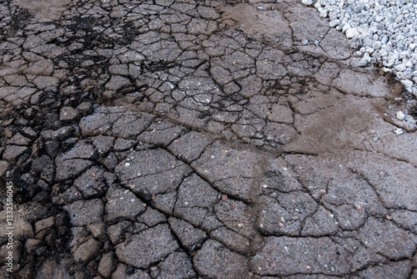 Fototapeta Cracked, dry asphalt surface with deep fissures and gravel on the side, showcasing natural textures. Ideal for construction, road repair, and environmental background concepts.