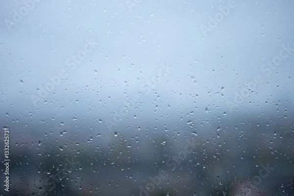 Fototapeta Raindrops on glass window with blurred cityscape in the background. Wet transparent surface covered with water droplets on a rainy day. Abstract weather and nature concept for design and print