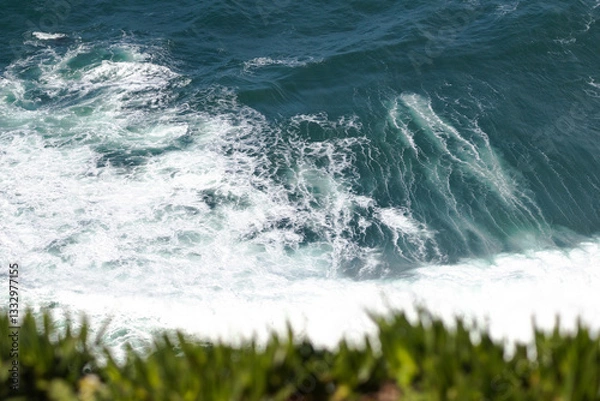Fototapeta Rocky Cape Roca in Sintra cliffs rise steeply from the Atlantic Ocean, covered with patches of greenery. Waves crash against the jagged shoreline, creating white foam contrasting.