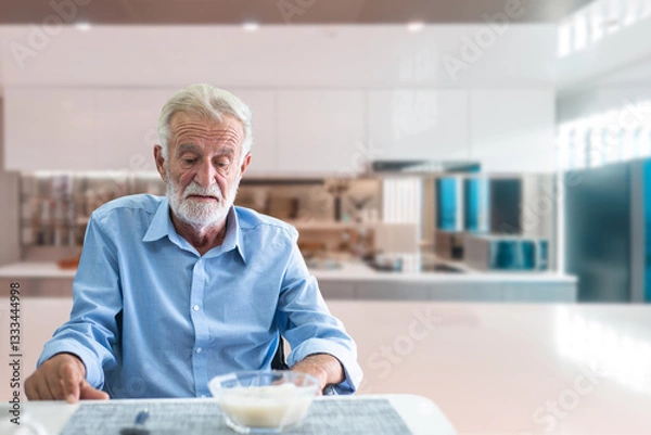 Fototapeta Senior man sitting quietly at a kitchen table, looking uninterested in his meal, representing poor appetite in older adults.