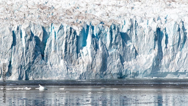 Fototapeta The image captures the stunning majesty of a towering glacier, with its blue and white hues reflecting in the calm waters below, illustrating the beauty of nature’s frozen wonders.