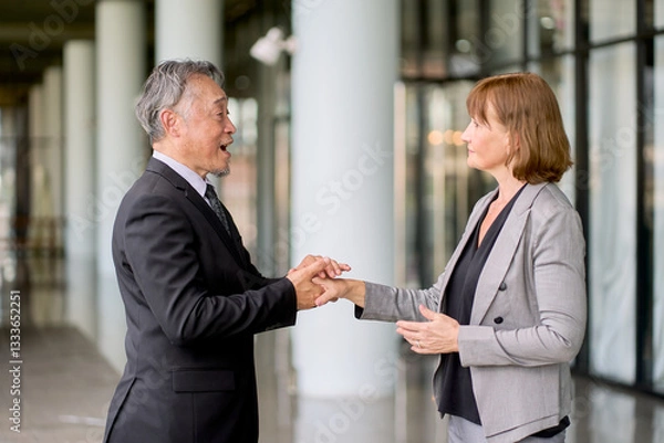 Fototapeta Two senior business people shaking hand together in formal suit and stand on company corridor area for commitment.