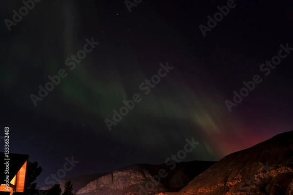 Fototapeta The stunning aurora borealis fills the night sky with vivid green and violet hues, captivating the viewer as it dances over mountains in this breathtaking natural display.