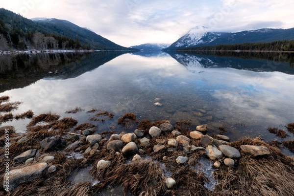 Fototapeta A tranquil mountain lake mirrors the surrounding landscape, featuring a rocky shoreline that enhances the peaceful atmosphere of the natural environment.